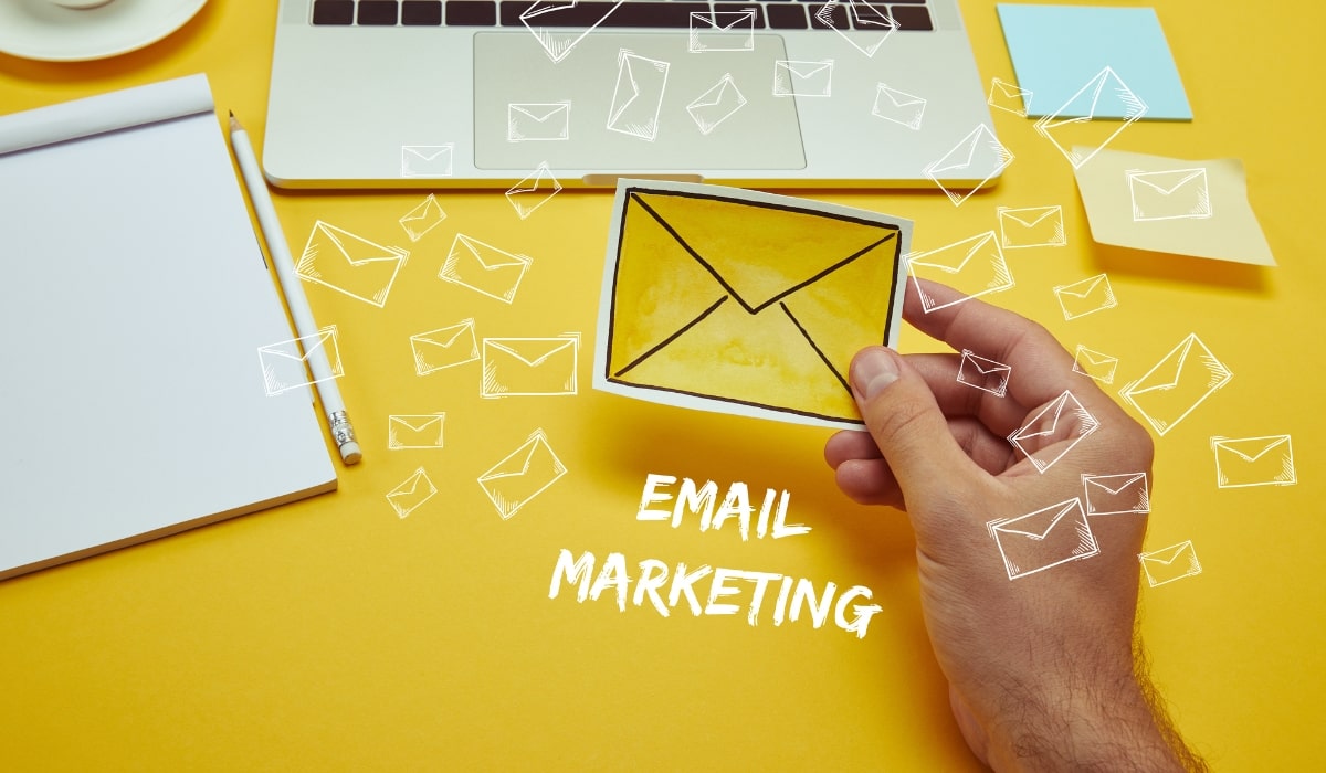 A laptop and a hand holding a small email envelope saying email marketing